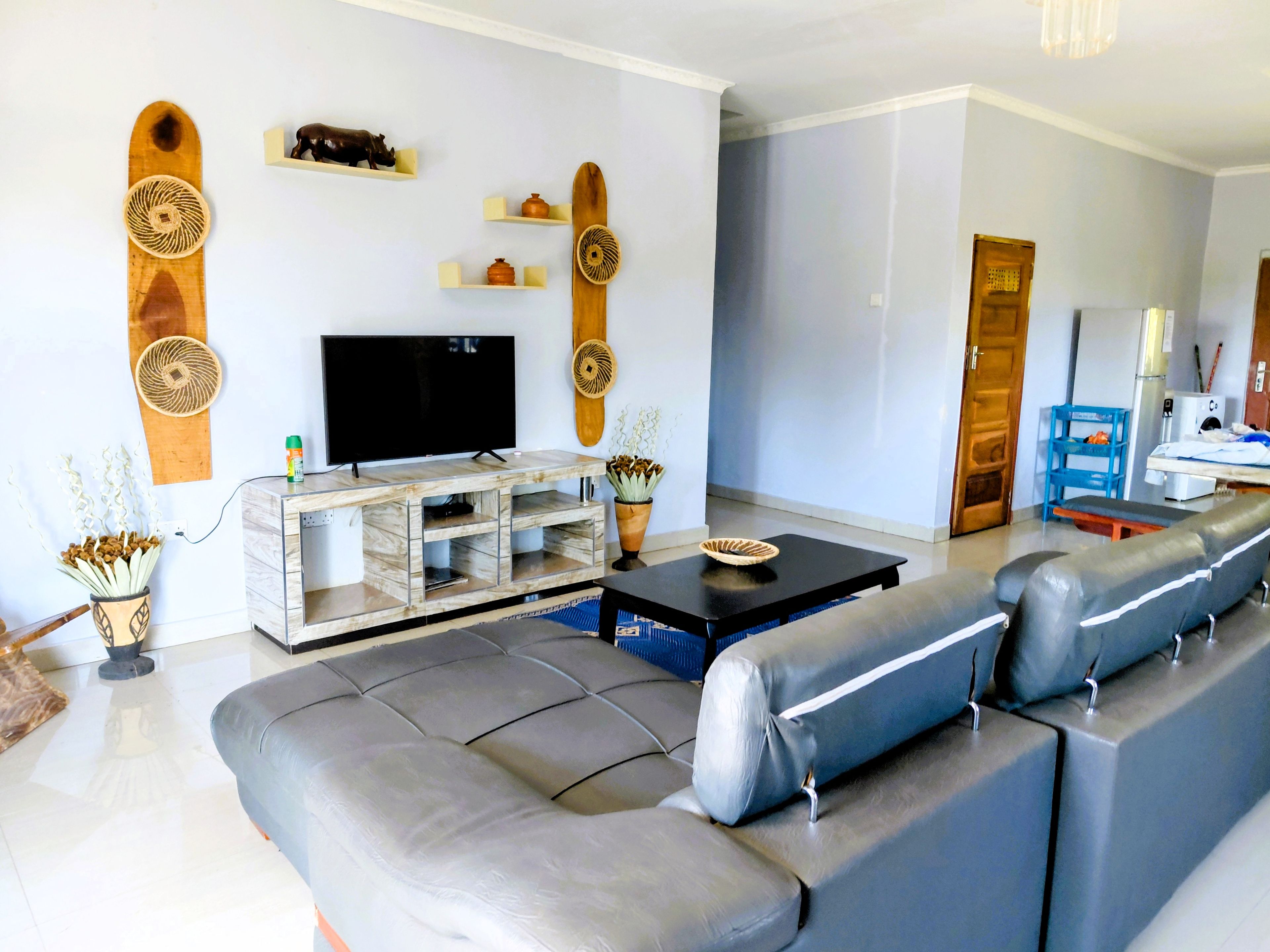 Een moderne woonkamer met een grijze bank, een televisie op een houten dressoir en decoratieve wandplanken.
