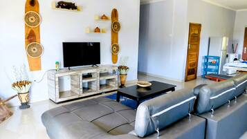 Een moderne woonkamer met een grijze bank, een televisie op een houten dressoir en decoratieve wandplanken.