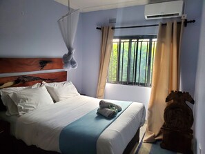 Una habitación de hotel con cama, ventana con cortinas, unidad de aire acondicionado y un cabecero decorativo.