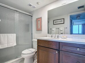 A bathroom with a shower, toilet, vanity with a mirror, and a window.