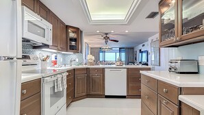 A modern kitchen with wooden cabinets, a built-in microwave, and a central island. - Beachfront Getaway at Caper Beach Club #204 | Private Chiller/Heated Pool (Fort Myers Beach)