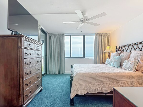 Un dormitorio con cama, cómoda, ventilador de techo y ventanas amplias.