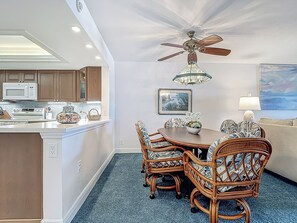 A dining area with a round table, six wicker chairs, a ceiling fan, and a chandelier.