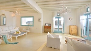 A spacious living room with a white sofa set, a wooden cabinet, and a chandelier. - Villa Irida (Mikonos)