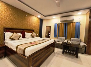 Una habitación de hotel con una cama grande, un sofá, una mesita y un aire acondicionado.