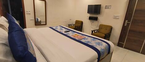 A hotel room with a bed, a flat-screen TV mounted on the wall, a desk with a chair, and a door.