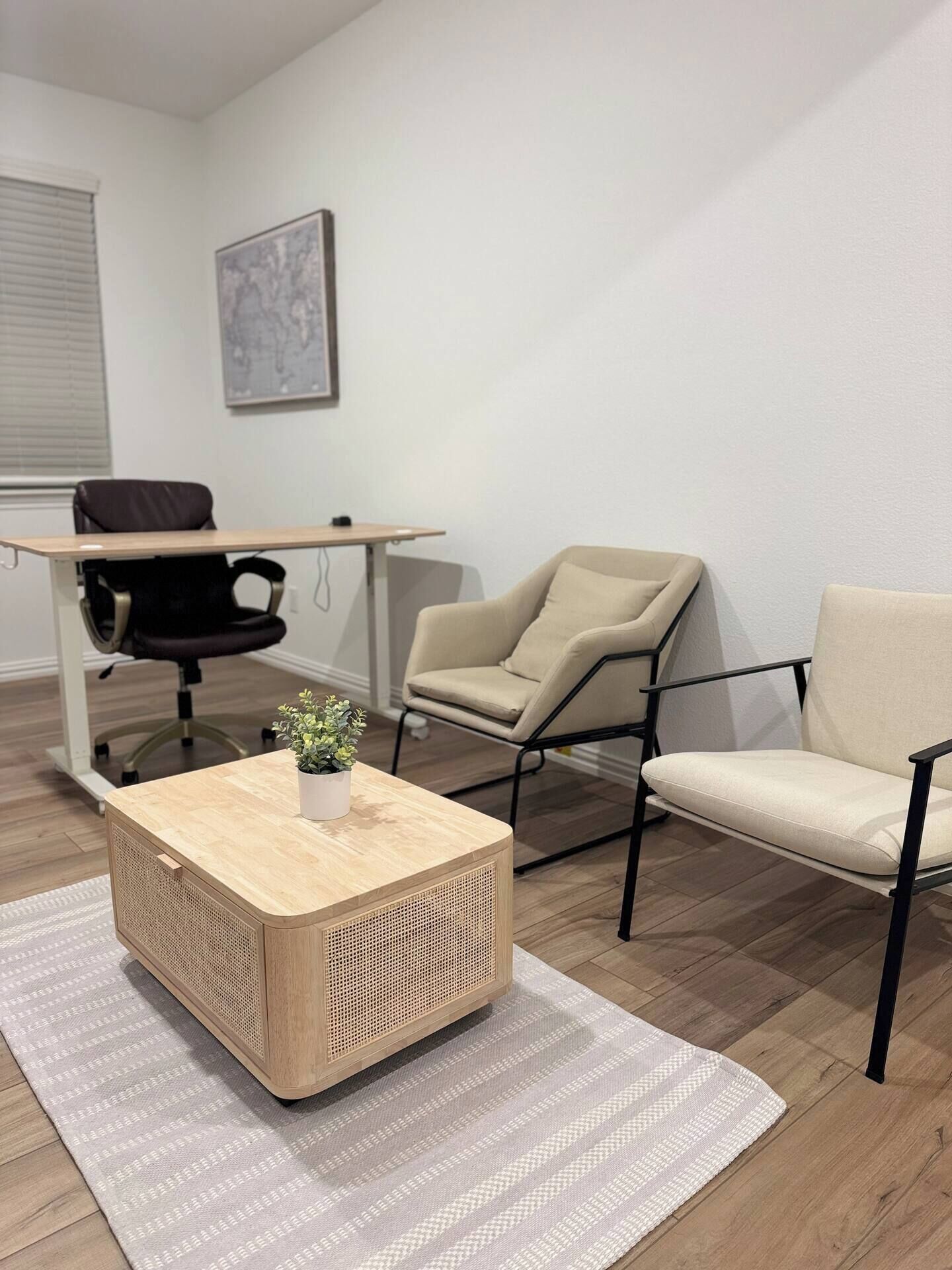 A modern office space with a wooden coffee table, two chairs, a desk, and a potted plant.