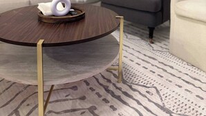 Ein runder Couchtisch mit weißer Vase und Pampasgras, ein graues Sofa und ein gemustertes Teppich im Wohnzimmer.