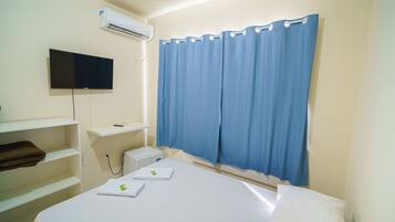Ein Hotelzimmer mit Bett, flachbildfernseher an der Wand, Schreibtisch mit Computer und blauem Vorhang.