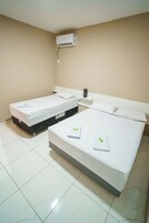 Quarto de hotel com duas camas, um ar condicionado branco e uma pequena mesa de cabeceira com abajur.