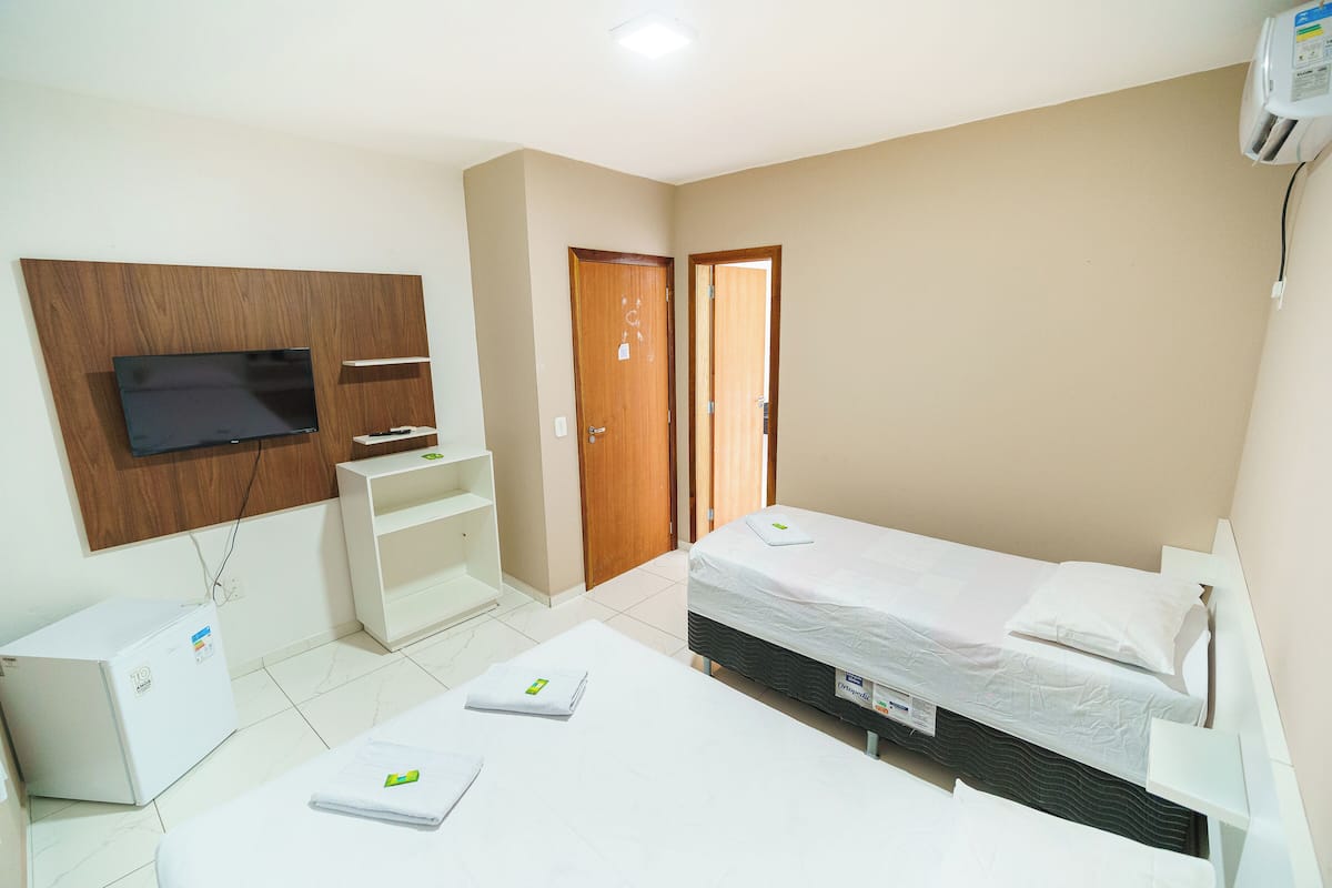 A hotel room with a bed, a TV mounted on the wall, a small desk, and a wardrobe.