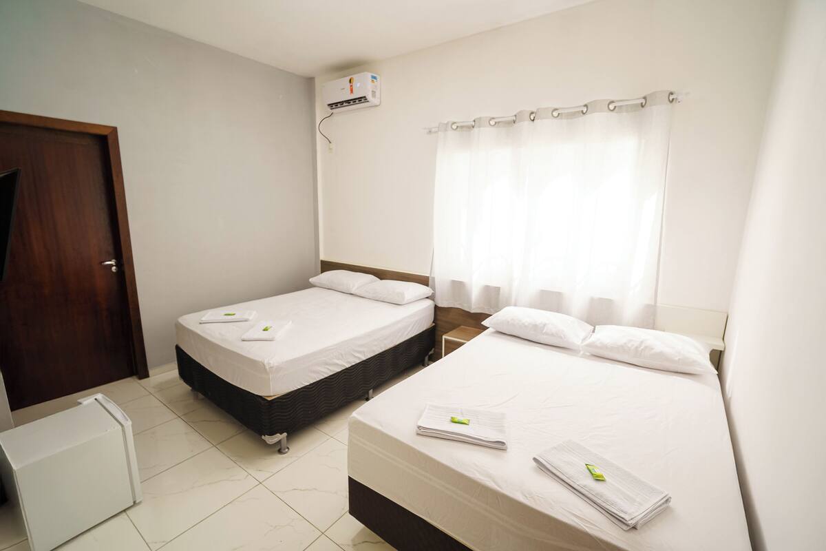 A hotel room with two single beds, a small bedside table, a wardrobe, and a window with curtains.