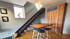 Eine moderne Küche mit Holztisch und Barhocker, einer Treppe mit Metallgeländer und einem Fenster mit Aussicht.