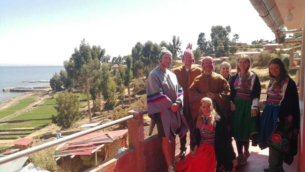 A group of people on a balcony overlooking a coastal landscape with a clear view of the sea and distant hills.