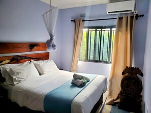 A hotel room with a bed, a window with curtains, an air conditioning unit, and a decorative headboard.