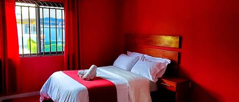 Una habitación con cama, mesita de noche y ventana con cortinas.