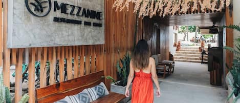 A wooden bench with a cushion, a sign with the name 'MEZZANNE', and hanging floral decorations.