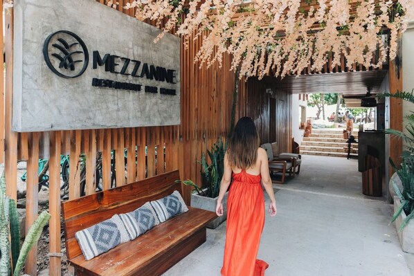 A wooden bench with a cushion, a sign with the name 'MEZZANNE', and hanging floral decorations.