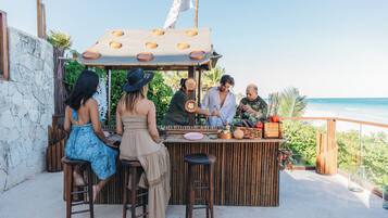 Zona de bar con taburetes y mostrador de madera, con vistas a una playa.