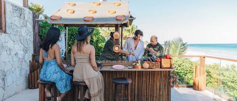 A bar area with stools and a wooden counter, overlooking a beach.