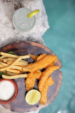 Una bandeja de madera con pescado frito, papas fritas y un gajo de lima.