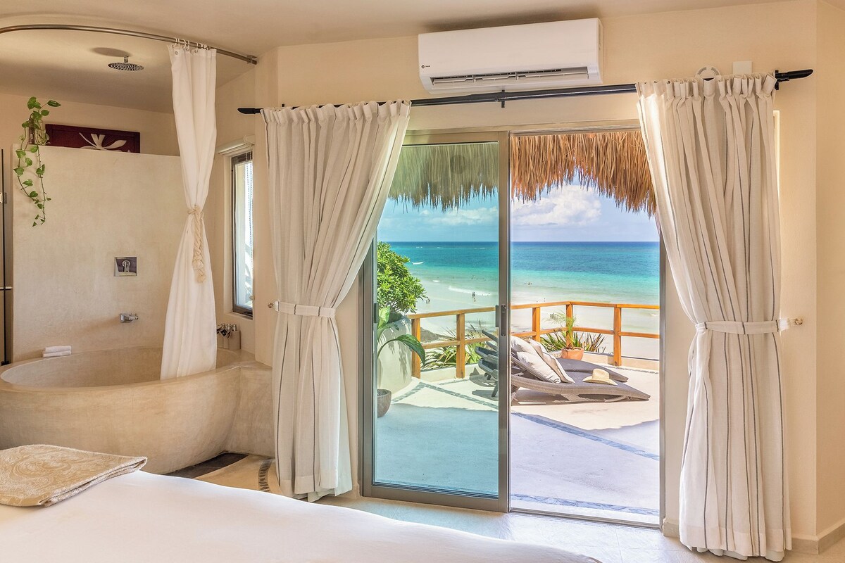 Quarto de hotel com banheira, cama e varanda com vista para a praia.