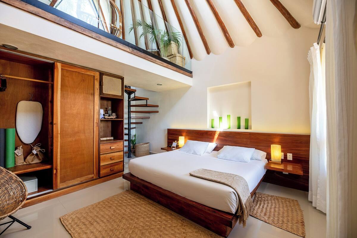 Une chambre avec un grand lit, une armoire en bois et un balcon agrémenté de plantes.