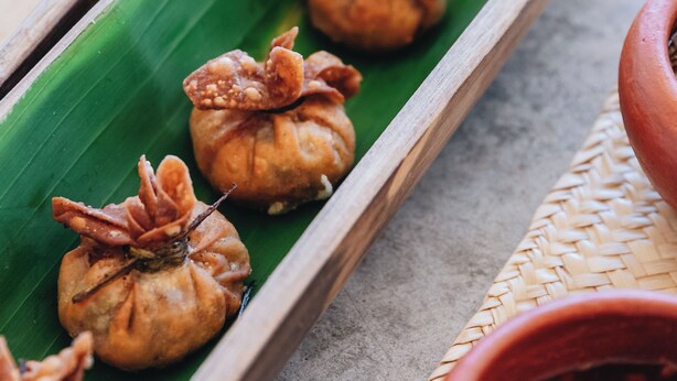 Une assiette contenant divers aliments, posée sur une feuille verte, accompagnée d’un petit bol de sauce.