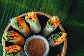A wooden tray with several spring rolls and a small bowl of sauce. - Mezzanine by La Zebra, an SLH Hotel (Tulum)