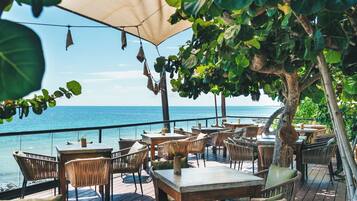 An outdoor dining area with tables and chairs, overlooking the sea.
