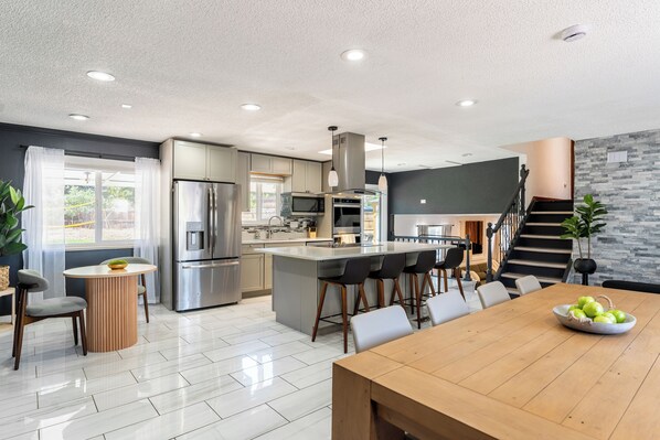 Una cocina moderna con una isla central, electrodomésticos de acero inoxidable y una zona de comedor con mesa y sillas de madera.