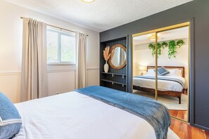 Un dormitorio con cama, ventana con cortinas, espejo y vista hacia otra habitación.