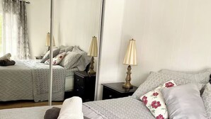 Ein Schlafzimmer mit einem großen Bett, einem Nachttisch, einer Lampe und einem Spiegel.