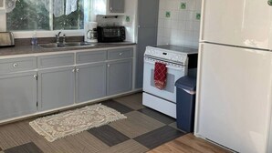 Eine Küche mit grauen Schränken, einem weißen Herd, einem weißen Kühlschrank und einem Fenster mit Spitzenvorhängen.