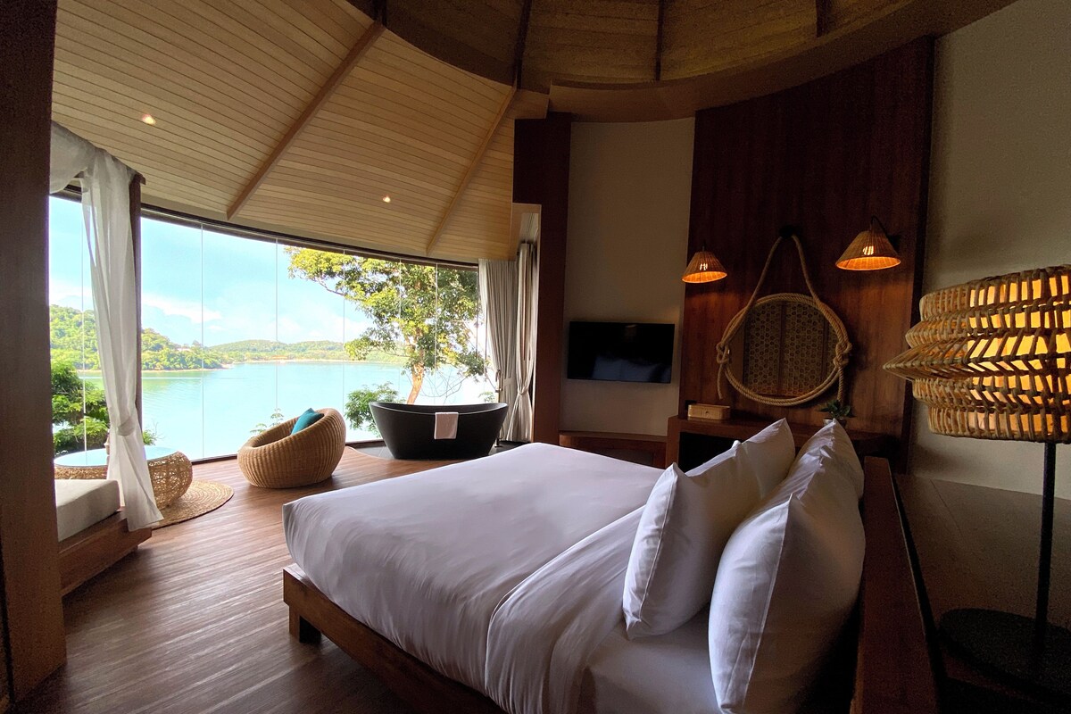 Een slaapkamer met een bed, een televisie, een raam met uitzicht op een meer en een plafondventilator.