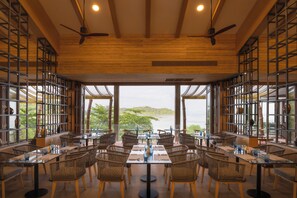 A restaurant with high ceilings, wooden beams, and large windows offering a view of the sea. - Sinae Phuket Luxury Hotel (Ratsada)
