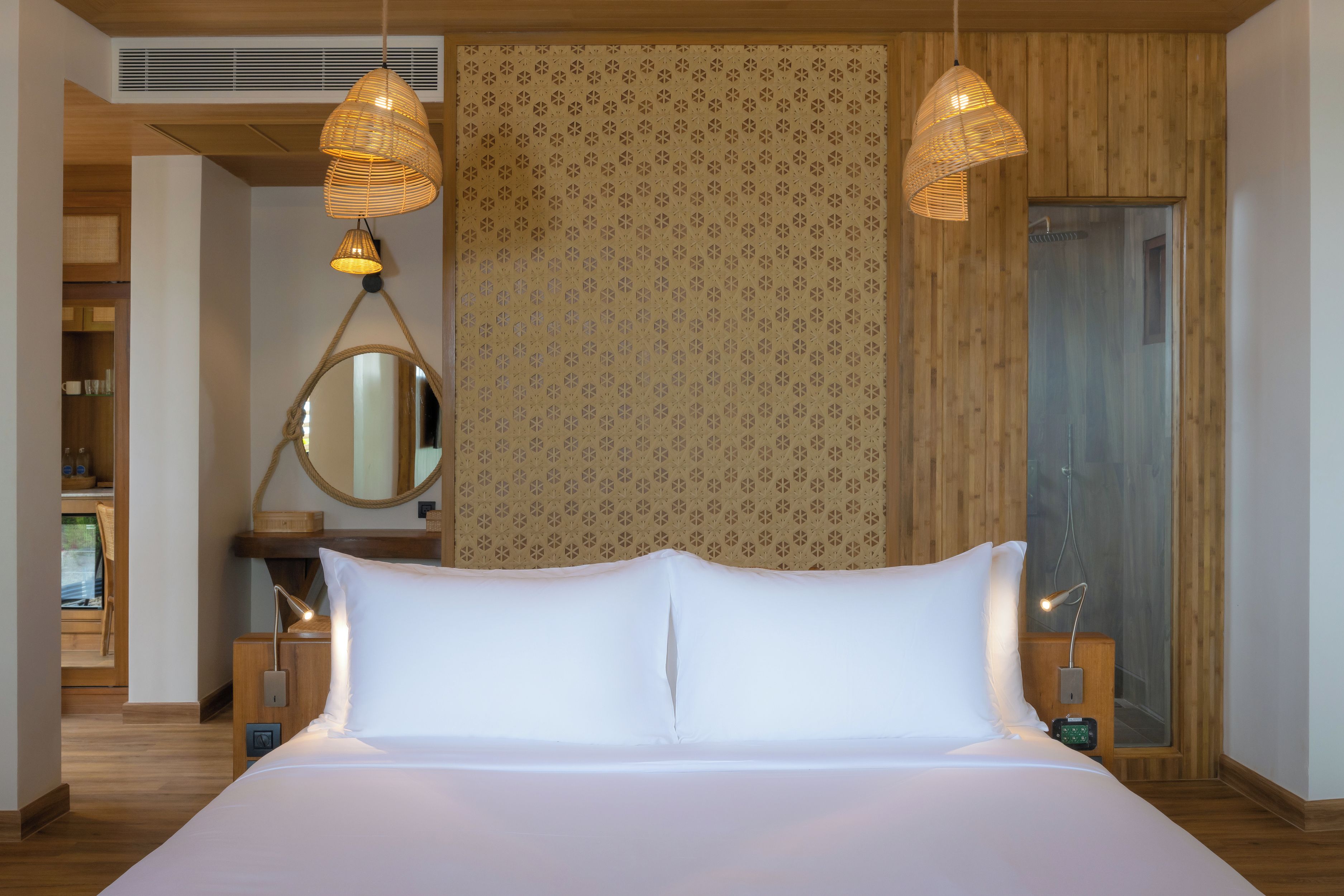 A neatly made bed with white linens, two bedside lamps, a bedside table, a mirror, and a patterned wall.