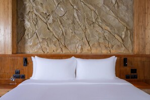Een bed met witte lakens, een houten hoofdbord en een textuurrijke stenen muur erachter.