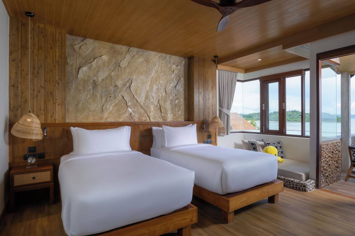 Een kamer met twee bedden, een stenen muur, houten plafond en een balkon met uitzicht.