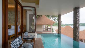 A poolside area with a wooden bench, a table, and a view of the sea.
