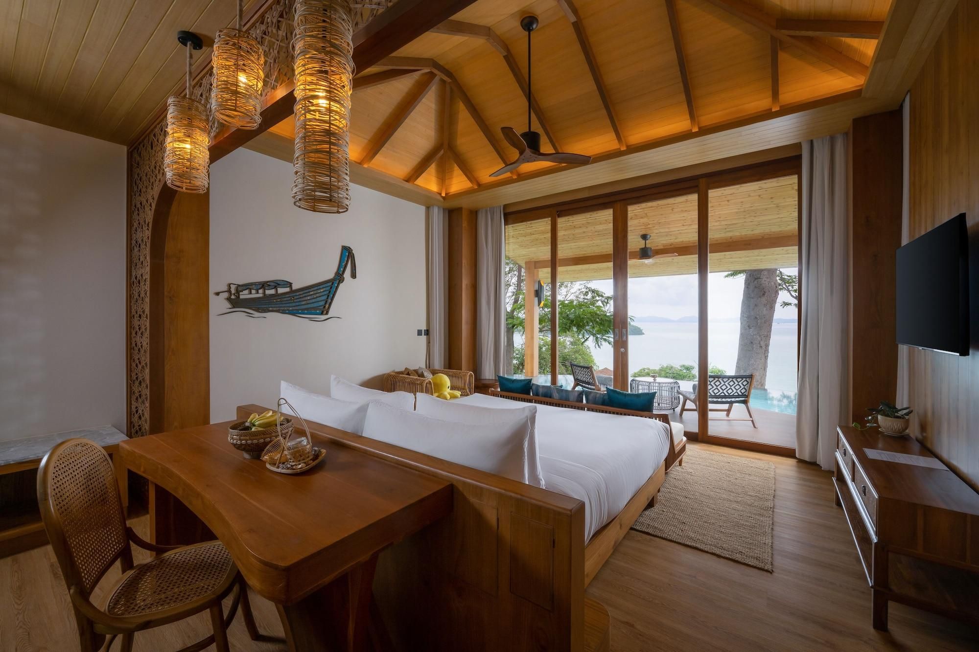 A room with a bed, a dining table, chairs, a TV, and a view of the sea.