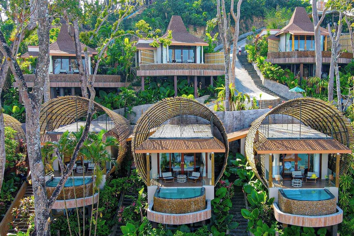 Een resort met meerdere bungalows, elk met een ronde houten constructie en een zwembad, omgeven door weelderige begroeiing.