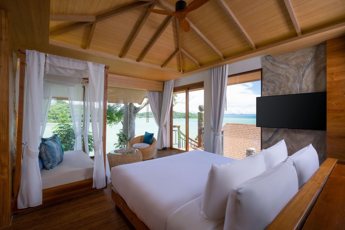 Een slaapkamer met een groot bed, een plafondventilator, een televisie en uitzicht op zee.