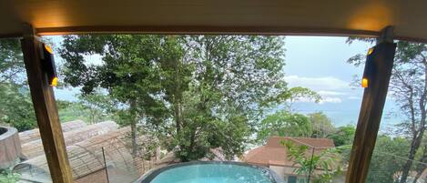 A pool area with two chairs and a table, surrounded by glass walls offering a view of trees and a distant landscape.