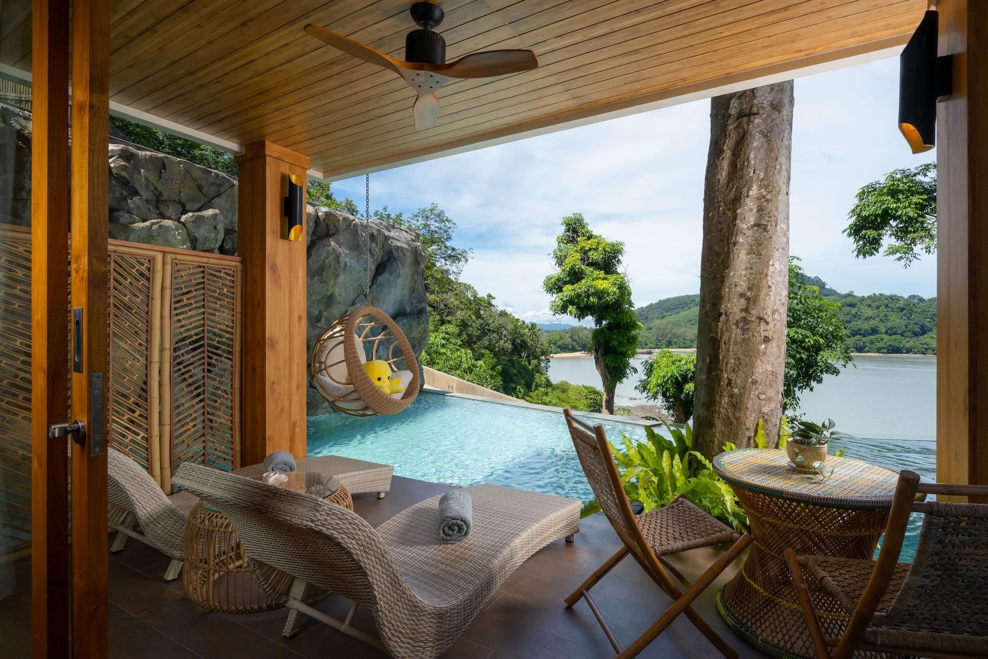 A poolside area with wicker furniture, a hanging chair, and a view of a lake and greenery.