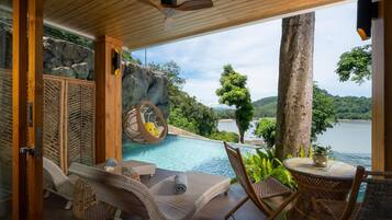 A poolside area with wicker furniture, a hanging chair, and a view of a lake and greenery.