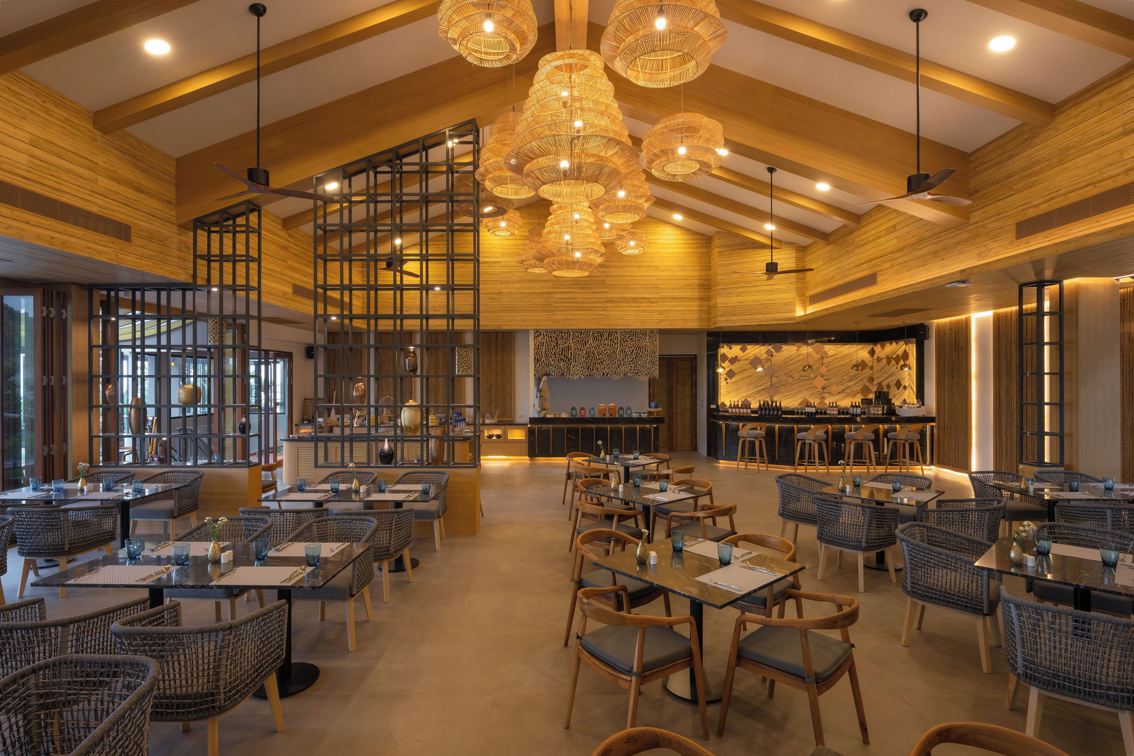 Interior de restaurante con techos altos, vigas de madera y mobiliario de mimbre moderno.