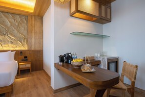 Une chambre moderne avec un lit en bois, une petite table de chevet, un comptoir-bar avec un saladier de fruits, une machine à café et une étagère en verre au-dessus du comptoir.