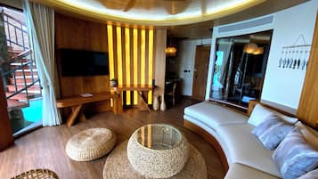 Un salon moderne avec un canapé aux lignes courbes, un téléviseur à écran plat, des éléments décoratifs en bois et un escalier.