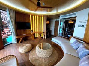 Un salon moderne avec un canapé aux lignes courbes, un téléviseur à écran plat, des éléments décoratifs en bois et un escalier.